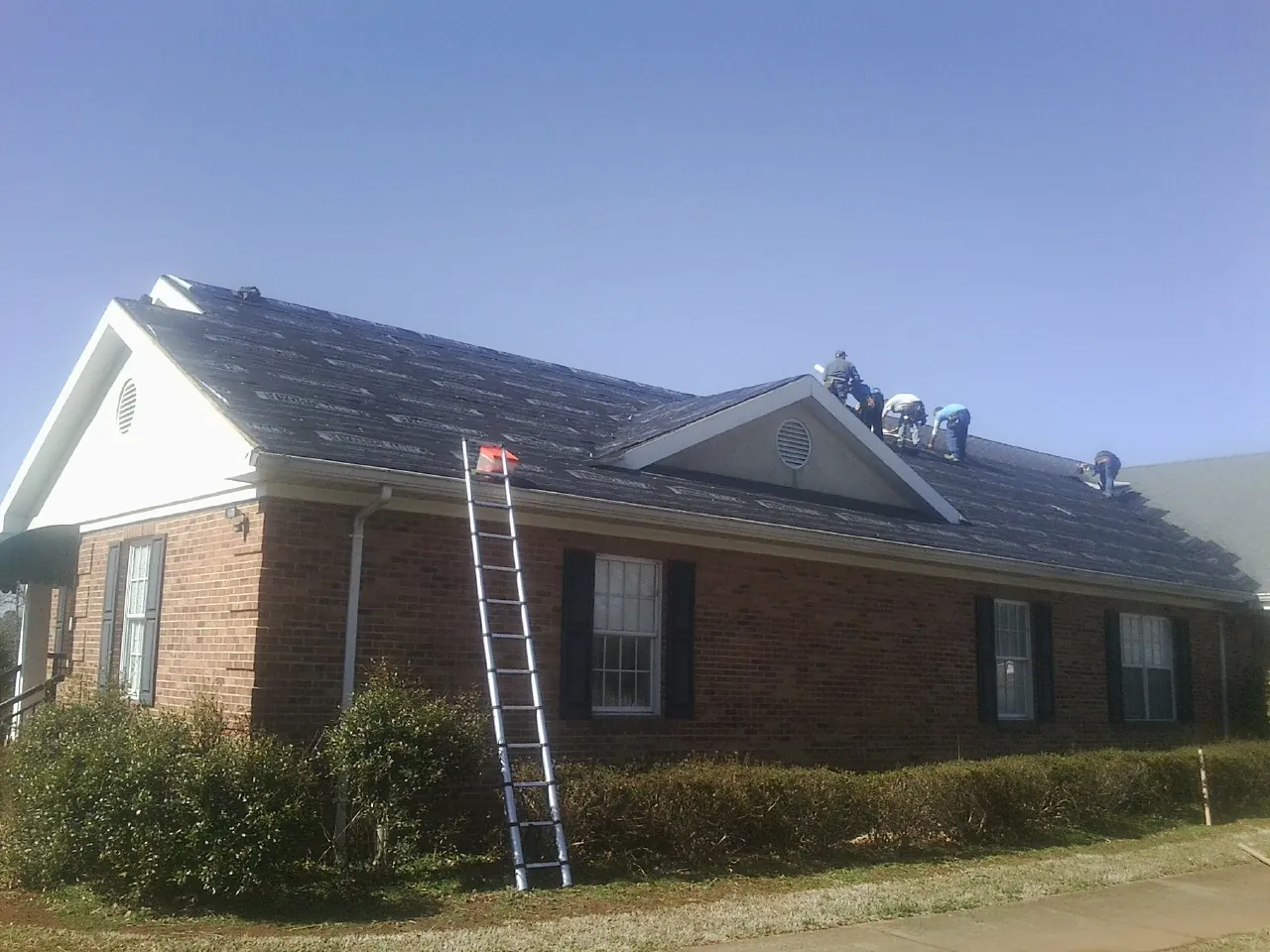 Crew tearing shingles off a brick ranch roof with a ladder set — Emergency Roof Repair work by our crew in Faucett