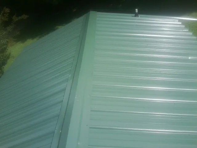 New green metal panels meeting at the ridge of a roof — Flat Roof Repair work by our crew in Faucett