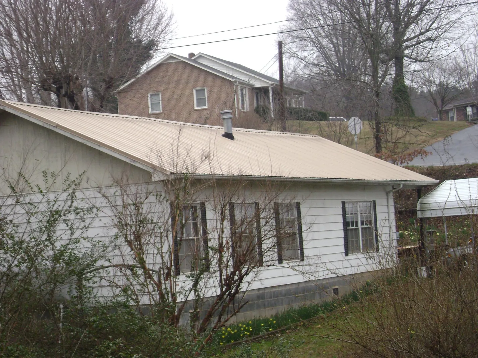 Tan metal roof on a white sided house set into a hillside — Commercial Roofing by Roofing Brothers in Faucett