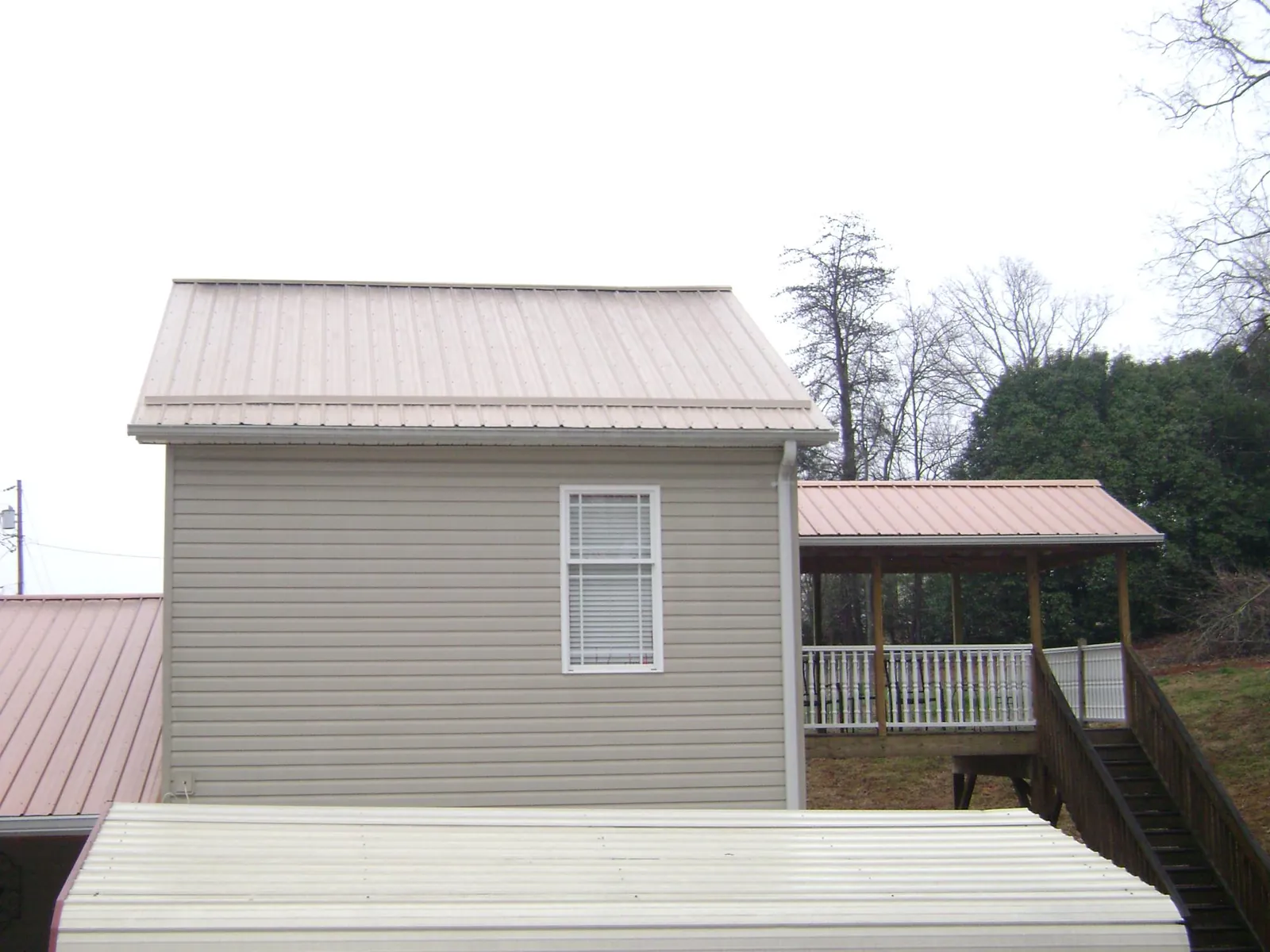Tan metal roofs on a two story addition and attached porch, from a Roof Replacement job in Faucett
